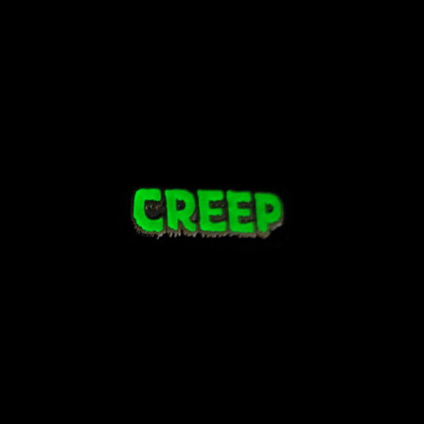 "CREEP" text glow-in-the-dark green and black enameled gunmetal finish metal lapel pin, shown glowing against black background
