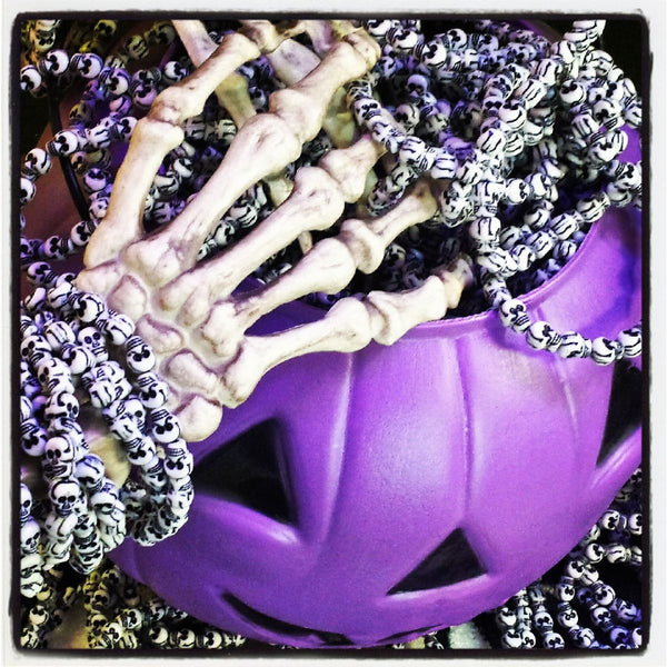 3/8" finely detailed white plastic with black shading two-faced skull beads on stretch filament bracelet, showing many in a purple halloween treat pumpkin bucket with skeleton hand