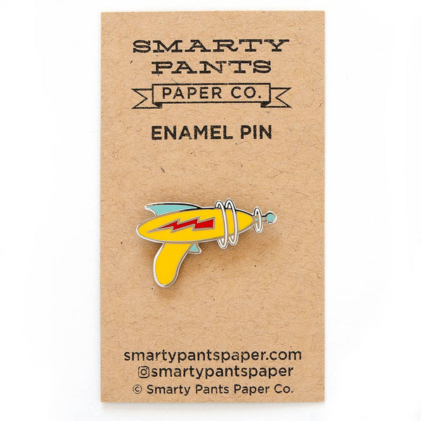 yellow ray gun emblazoned with red electricity bolt enameled silver metal lapel pin, shown on illustrated cardstock backer packaging