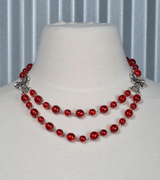 linked translucent round red beads 17" chain necklace with double strand center section anchored by silver metal bows, shown on display form