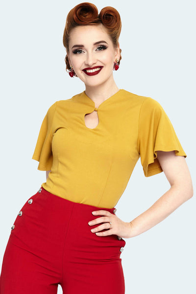 A model wearing a mustard colored knit top with flutter style short sleeves and a keyhole detail neckline. The top is tucked into a pair of pants