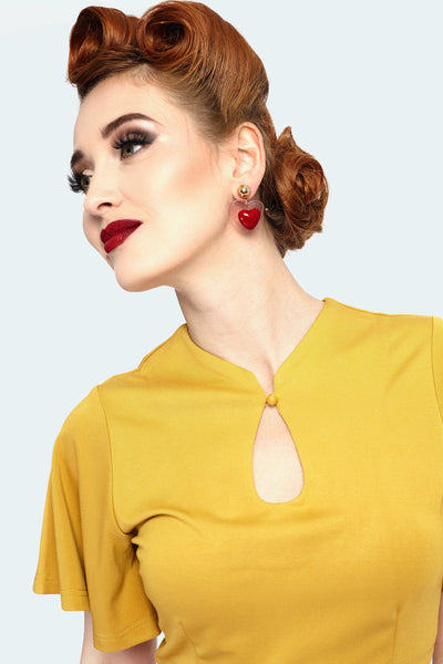 A model wearing a mustard colored knit top with flutter style short sleeves and a keyhole detail neckline.  Shown in close up to feature the flutter sleeves and keyhole detail
