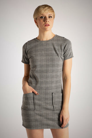 A model wearing a short sleeved micro-mini jersey dress in a grey tartan style. It has two pockets