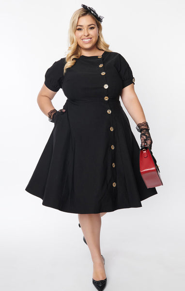 A black short sleeved dress with a high neck and full skirt. It has clear buttons with gold starburst detail down the front and on each sleeve. Shown on a plus sized model