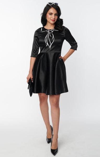shiny stretch black satin dress featuring a Trompe l'oeil "painted on" scarf and collar printed in contrast bright white, fitted round neckline bodice, 3/4 sleeves, and full just-above-the-knee length skirt, shown on model