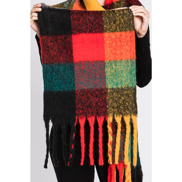 model wearing a thick knit scarf with fringe ends in a orange, red, mustard, teal, and black oversized plaid pattern. shown pulled flat