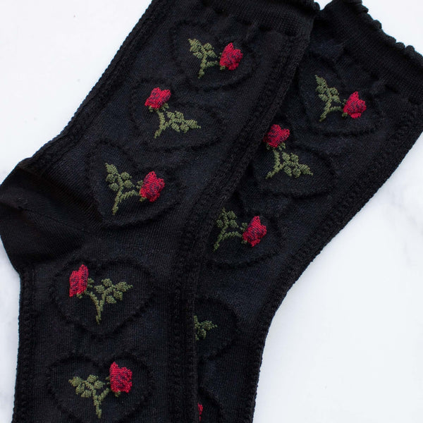 Cozy cotton knit socks in black with an all-over knit-in pattern of a rose with its stem inside of a scalloped heart. Ruffled cuff in matching black. Shown in close up