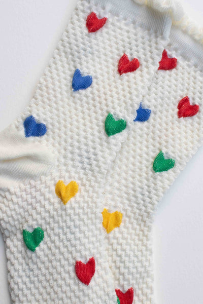 white cotton socks with waffle texture knit, ruffled cuffs, and knit-in pattern of red, blue, green, and yellow hearts. Shown in close up