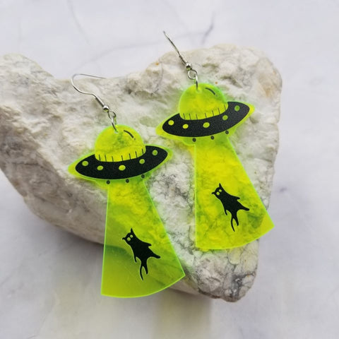 laser cut translucent neon green acrylic dangle earrings with printed detail of a black UFO pulling a black cat towards it with a tractor beam