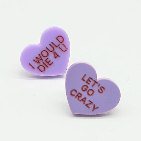 Pair of acrylic resin post earrings in pale purple with laser cut written message in red “I WOULD DIE 4 U” on one earring and “LET’S GO CRAZY” on the other. Shown flat
