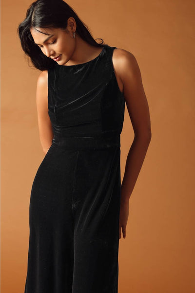 model wearing black velvet jumpsuit with boatneck and seamed sleeveless bodice, banded waistband, and wide legs. Shown from front in close up