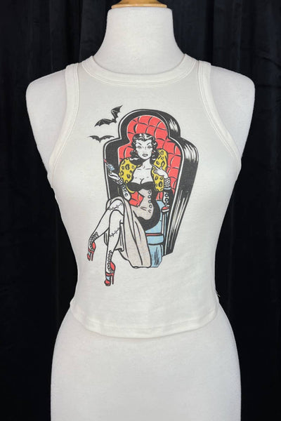 off-white ribbed tank top with round neck and printed illustration of pinup style woman with stitched legs wearing gown and sitting in coffin-style large chair. Printed in red, black, blue, and yellow. Shown on dress form