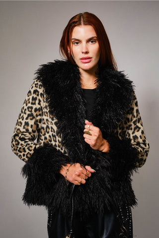 Woman wearing a leopard print coat with a black shaggy fur collar, cuffs, and bottom hem against a gray background. Shown from front