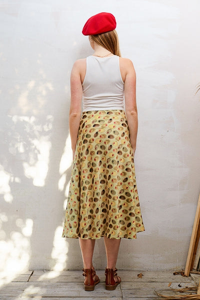 model wearing a silk weave midi skirt with elastic waistband and side slit in bright green and pimento stuffed olive pattern on light green background. Shown from back