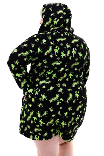 plus size model wearing a black long sleeve hooded onesie with neon green insect pattern, front zip closure, and mid-length shorts. Shown from back with hood up