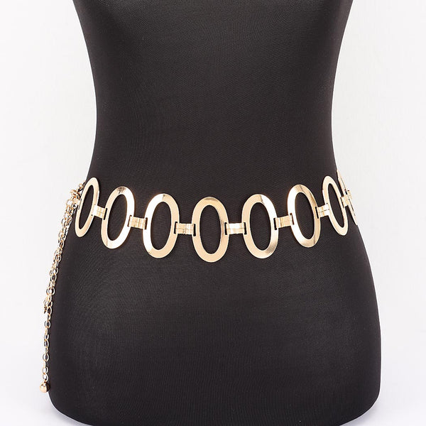 A gold metal chain belt with large flat oval links and a dangling chain extender, shown from the front on a black mannequin torso against a white background.
