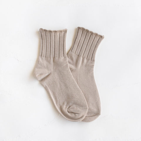Light beige cotton knit socks with ribbed pattern and scalloped cuffs. Shown flat