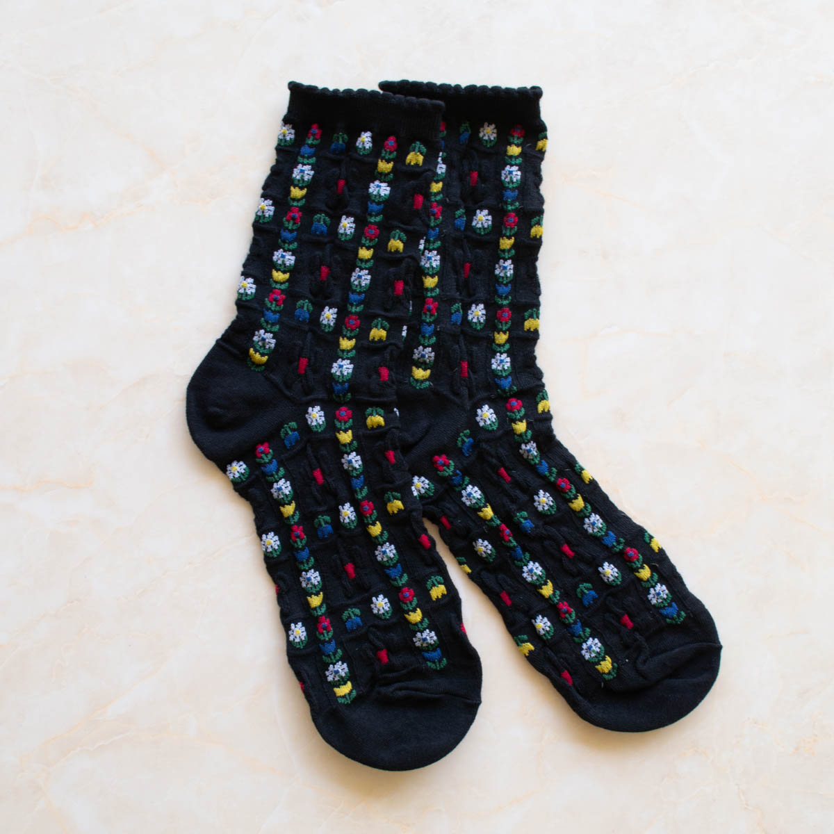 cotton knit socks in black with an allover red, yellow, green, blue, and white daisy and tulip knit-in pattern