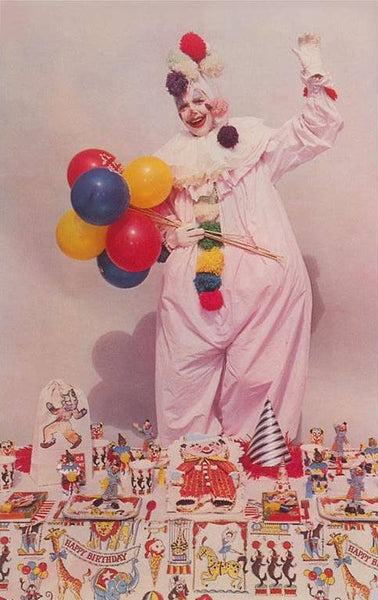 postcard of a vintage color photograph of a clown holding balloons in front of a collection of circus themed toys