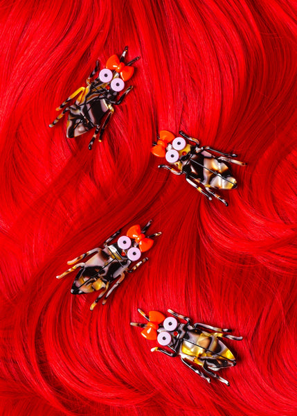 four acrylic brown swirled cockroach-shaped hair clip with large light pink eyes, red bow attached to antennas, and red rhinestone nose. Shown in bright red hair