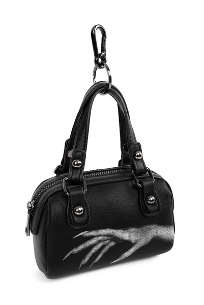Black faux leather mini purse shaped bag charm with white printed design of vampiric hand with long nails. Bag has gunmetal hardware, zip closure, and split ring keychain with clasp. Shown from front