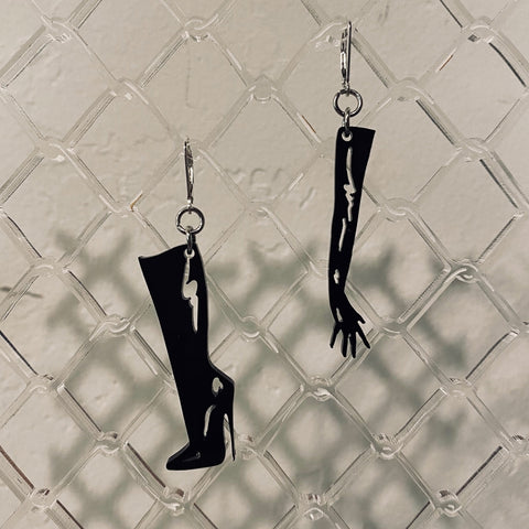 Black high-heeled boot and long glove-shaped earring set on a textured gray background