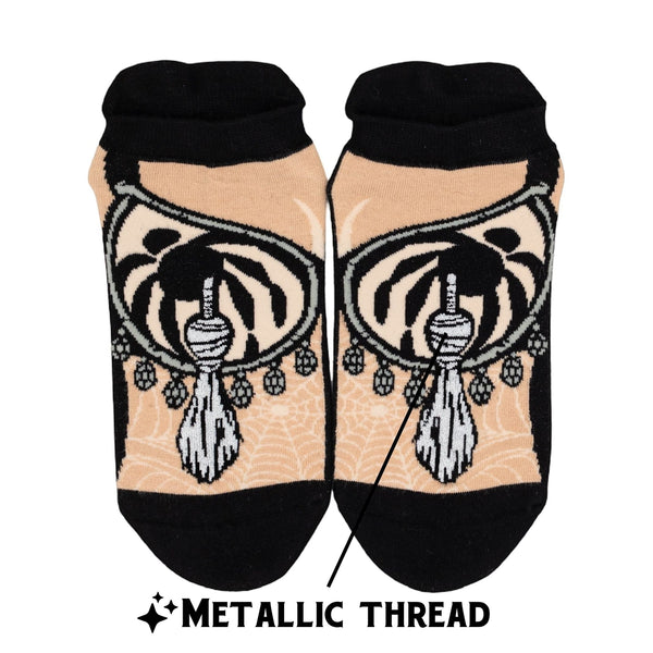 pair of ankle socks in beige with black toes, heels, and cuffs and image of Elvira's chest with bra and silver lurex pasties on each sock. Shown flat