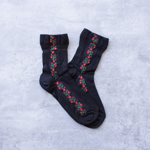 Black cotton socks with a knit-in pattern of red and green flowers and panels of patterned mesh. Shown flat