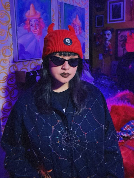bright red ribbed knit beanie with matching black devil horns shown worn by model with sunglasses