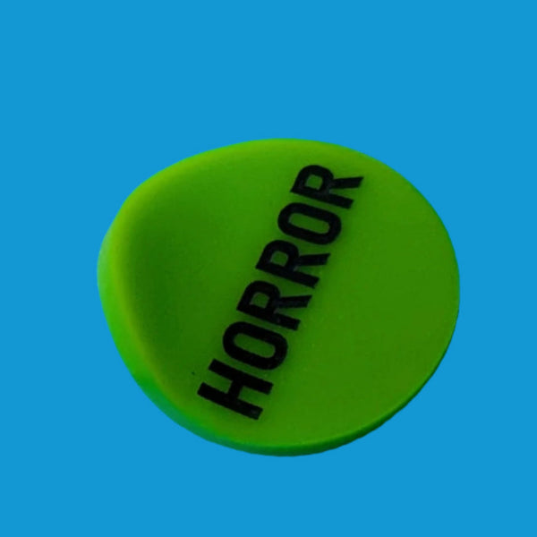 round neon green acrylic brooch with slightly concave shape and "HORROR" in black shown on neon blue background from side to show shape