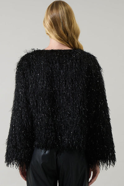 model wearing black shaggy faux fur cropped jacket with metallic fringe throughout. Jacket is collarless. Shown from back