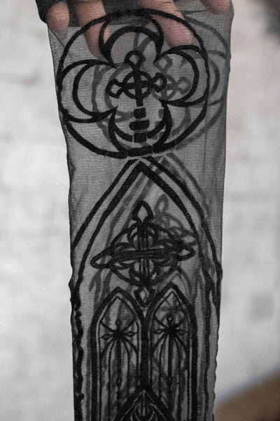 sheer stay up thigh highs with all over flocked pattern of cathedral arches. Shown held in close up to display flocked detail