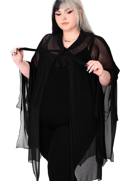 Plus size model wearing a black mesh cape with raw scalloped hemline in the shape of bat wings with sewn in arm holes and a self adjustable front tie. Shown from the front with self tie held taut 