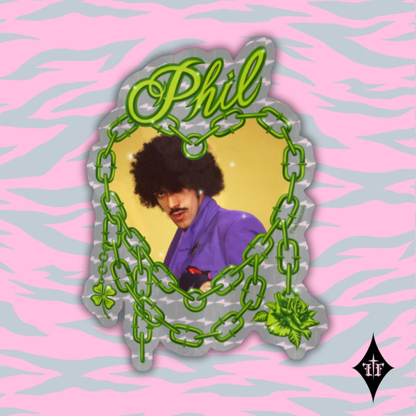 Holographic die-cut vinyl sticker featuring a portrait of Phil Lynott from Thin Lizzy wearing a purple shirt on a yellow background inside of an illustration of a neon green chain link heart with “Phil” in green script. Shown on pink and blue tiger print illustrated background