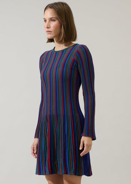 model wearing a fully lined sweater dress in a vertically striped ribbed pattern in jewel tones of blues, reds, greens, and amber. Dress is a mini length with flared skirt and slightly flared cuff long sleeves. Shown from side