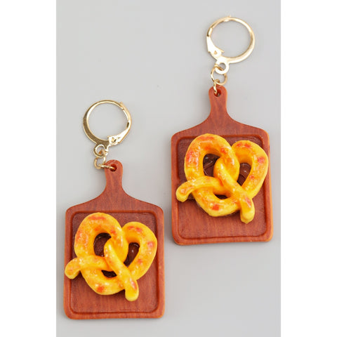 Acrylic dangle earrings with hinge back ear wires in the shape of wooden cutting boards with a large golden pretzel on each