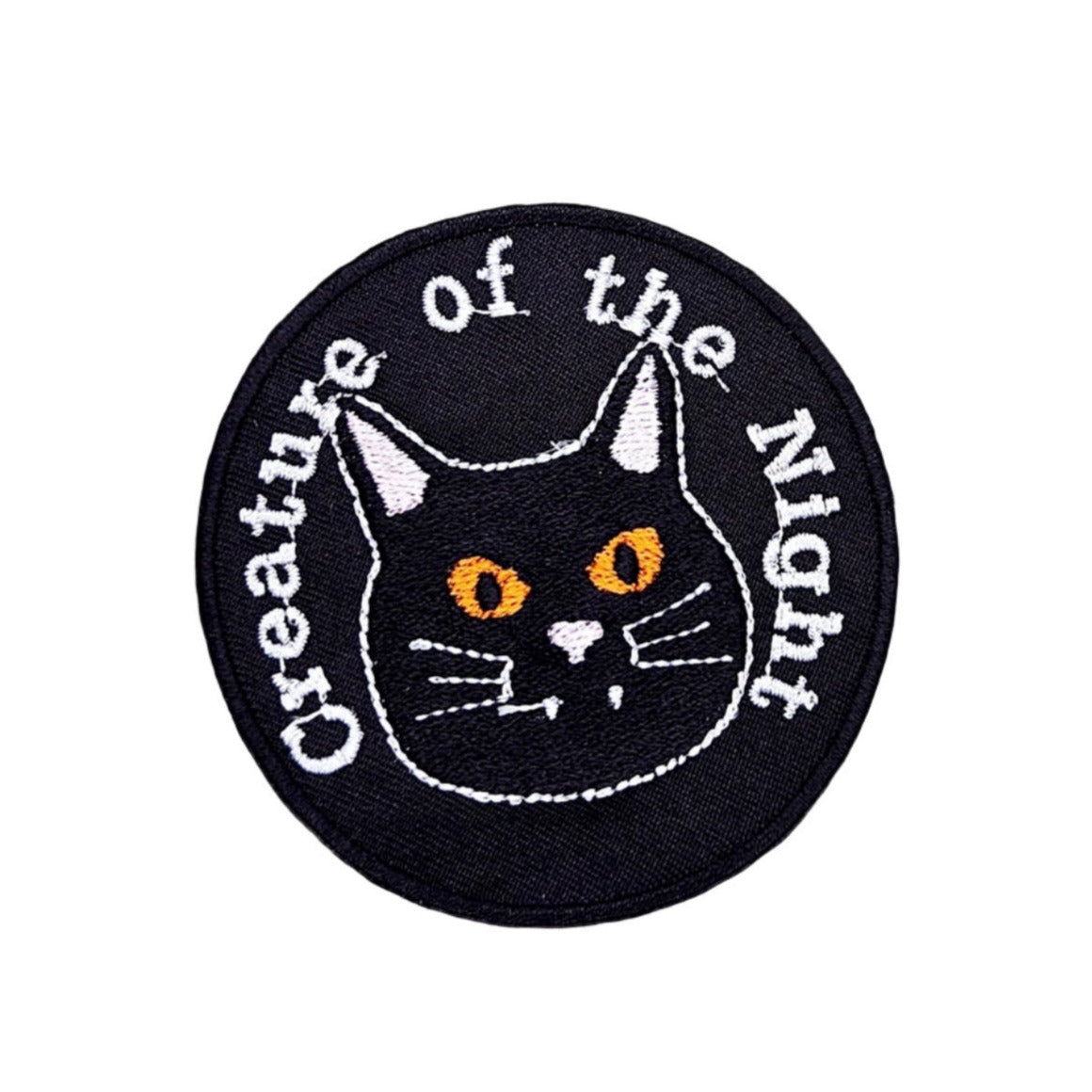Black cat with orange eyes on round black embroidered twill patch with message “Creature of the Night”