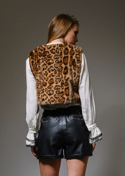 Woman wearing a leopard print vest over a white shirt on a gray background. Shown from back
