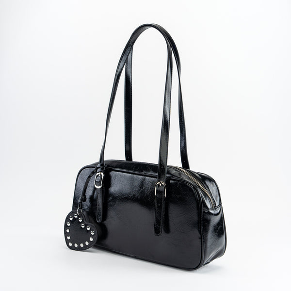 shiny black textured faux leather bowler bag with adjustable shoulder straps, sturdy silver metal zip closure, and studded matching faux leather heart-shaped mirror bag charm. Shown from side