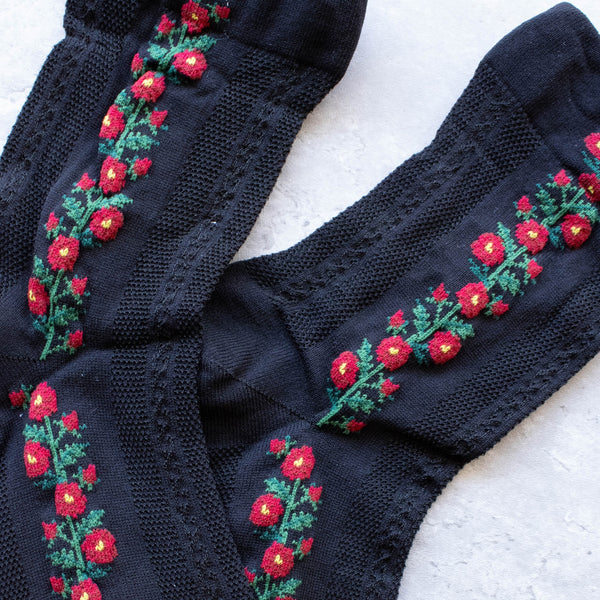 Black cotton socks with a knit-in pattern of red and green flowers and panels of patterned mesh. Shown flat in close up