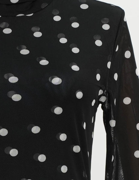 model wearing a black mesh turtleneck top with an allover print of white polka dots. Shown from front in close up of mesh fabric