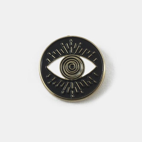 round gold metal enamel pin of an abstract illustration of an eye with a swirly hypnotic iris on a black background. Shown flat from the front