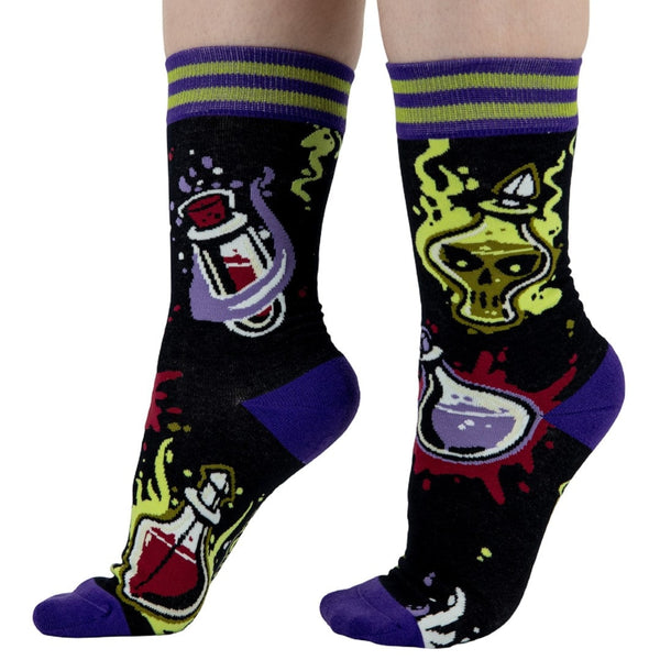 unisex cotton crew socks with all-over pattern of vials and potions surrounded by green and purple smoke with purple toes and heels and green & purple striped cuffs. Shown worn by model from side