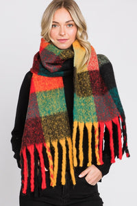 model wearing a thick knit scarf with fringe ends in a orange, red, mustard, teal, and black oversized plaid pattern