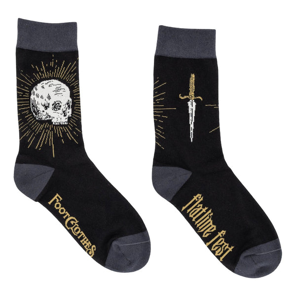 A pair of black cotton crew socks with dark gray cuffs, heels, and toes and design of white skull surrounded by golden yellow sunburst on one ankle and golden handled dagger on the other. Shown flat