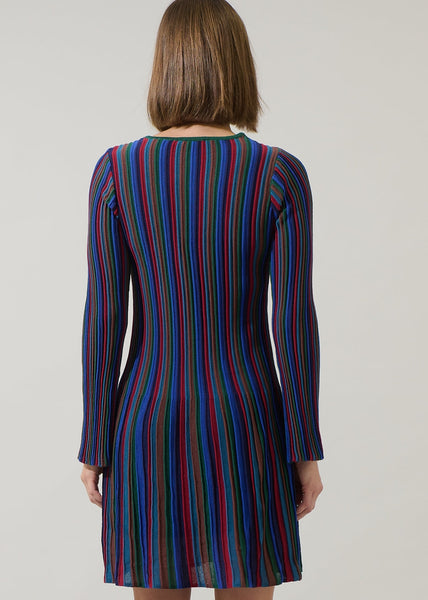 model wearing a fully lined sweater dress in a vertically striped ribbed pattern in jewel tones of blues, reds, greens, and amber. Dress is a mini length with flared skirt and slightly flared cuff long sleeves. Shown from back