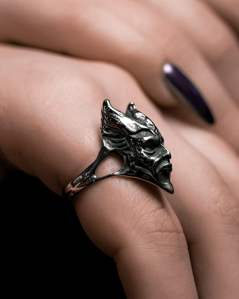 Model wearing stainless steel ring in the shape of a demon with pointed horns and face in angry expression with closed mouth. Seen from the right side angle