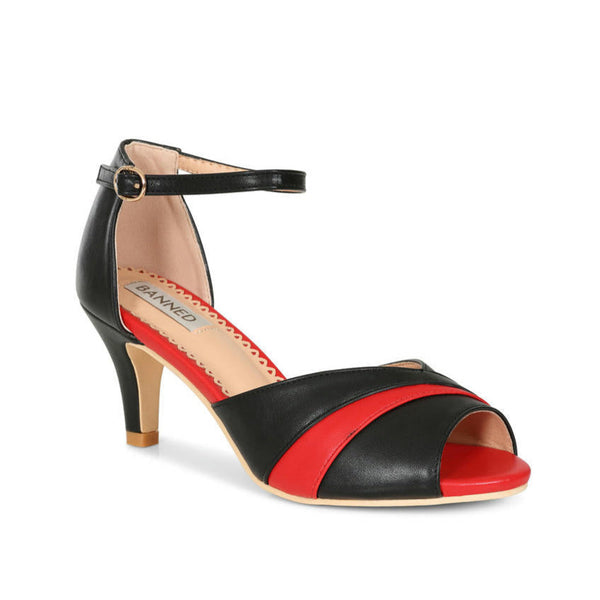 a pair of faux leather peep-toe heels with black and red striped toe strap, black ankle strap with gold metal buckle, and red insole. shown from three quarter angle