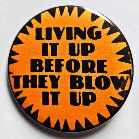 1.25” round button with bright orange starburst background and “LIVING IT UP BEFORE THEY BLOW IT UP” written in black
