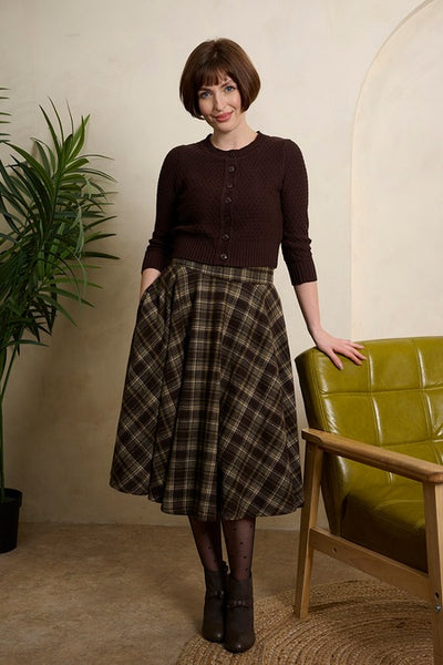 A woman modeling a dark brown button-up cardigan and a high waisted wool blend full circle swing skirt in deep brown, beige, yellow, and blue plaid pattern with side seam pockets. Shown from front